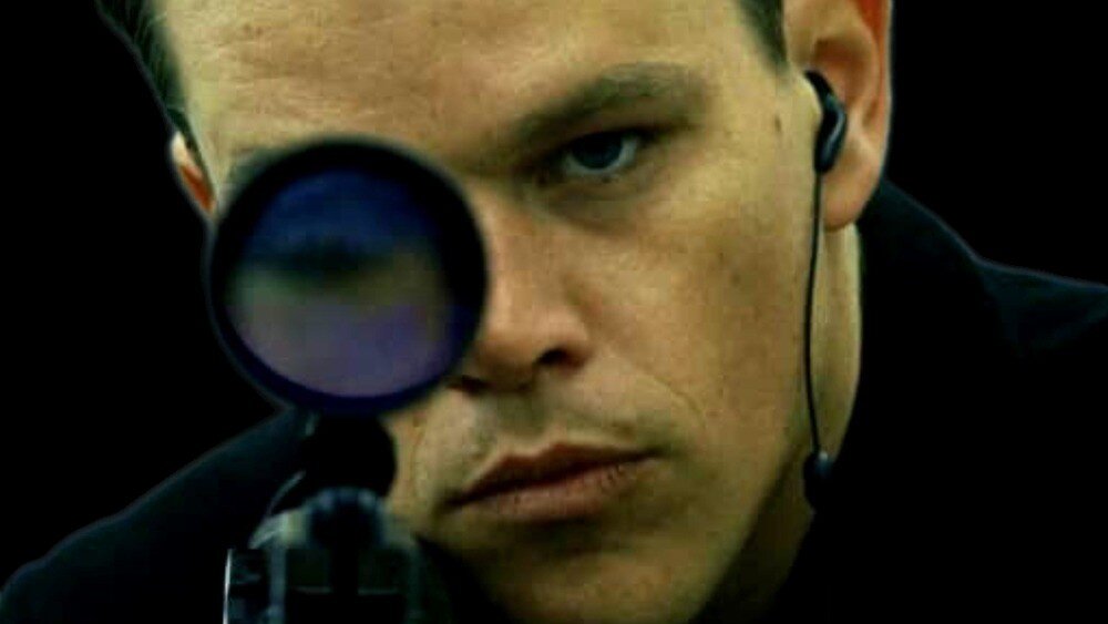 Film still of a man squinting through a large magnifying glass.